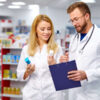 157826734-two-young-caucasian-colleagues-in-white-medical-gown-pharmacists-fulfilling-a-prescription-holding-m